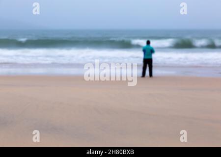 Rückansicht eines Mannes, der im November am Strand von Luskentire, Isle of Lewis and Harris, Äußere Hebriden, Schottland, Großbritannien, an der Küste stand - die bildende Kunst verschwommen Stockfoto