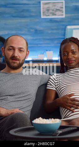 Schwanger interracial paar mit Videokonferenz für Remote-Online-Kommunikation zu Hause. Menschen mit gemischter Rasse, die ein Baby erwarten und mit Freunden mit Technologie im Wohnzimmer sprechen Stockfoto