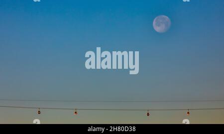 Ein schwindender Vollmond über der Emirates Air Line, auch bekannt als Dangleway, ist eine Seilbahn, die über die Themse in London, England, Stockfoto