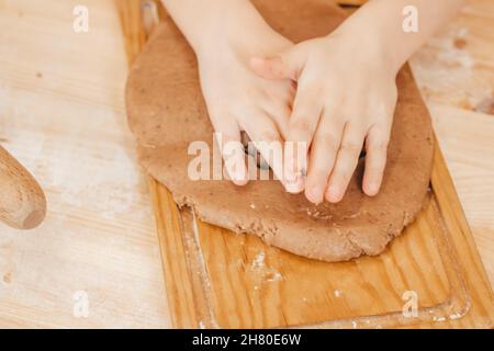 Mädchen rollt Ingwerteig mit ihren Händen aus. Mädchen bereitet weihnachtskekse auf einem Holztisch zu Stockfoto