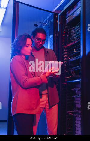 Interrassische Ingenieure verwenden digitale Tablets, während sie den Server im Rechenzentrum überprüfen Stockfoto