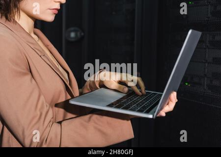 Beschnittene Ansicht des Programmierers, der Laptop verwendet, während er in der Nähe von Servern im Rechenzentrum arbeitet Stockfoto