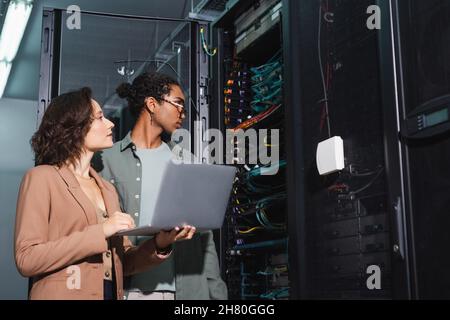 Junge interrassische Ingenieure mit Laptop, die die Diagnose des Servers im Rechenzentrum durchführen Stockfoto