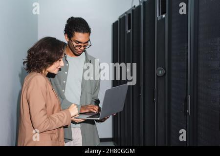 Junge interrassische Ingenieure, die im Rechenzentrum einen Laptop verwenden Stockfoto
