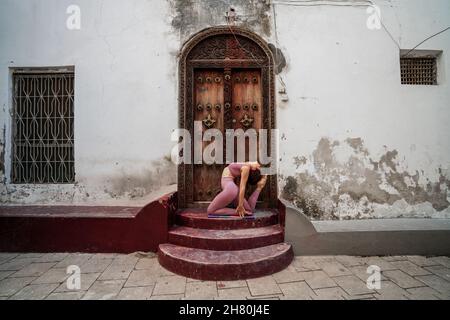 Gymnastikerin, die im Hof vor einer alten Holzhaustür Yoga macht Stockfoto