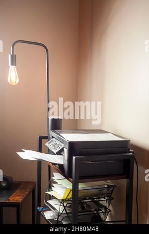 Kleines Heimbüro oder Kubik mit einer Stehleuchte, einem Bücherregal und einem Druckerscanner darauf. Es gibt mehrere Ordner und Papiere in Organisatoren im Stockfoto