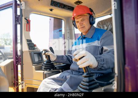 Glücklicher Fahrer Mann von industriellen Muldenkipper sitzt in der Kabine und arbeitet auf der Baustelle. Stockfoto