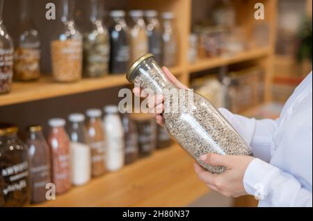 Eine Frau hält ein Glas Sonnenblumenkerne in der Hand. Verkauf von Schüttgütern nach Gewicht in einem Ökoladen. Stockfoto