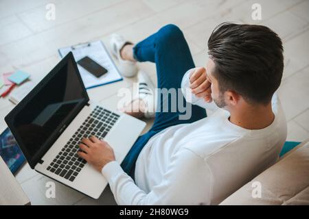 High-Angle-Aufnahme eines Mannes, der am Computer im Internet surfen konnte. Zu Hause auf dem Boden sitzen. Online-Technologie, Fernarbeitskonzept. Stockfoto