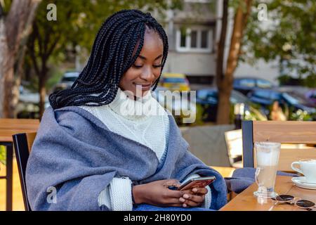 Schönes Mädchen, das sich in einem Café entspannt und in sozialen Netzwerken auf ihrem Handy chattet. Freizeit, Technologie und urbaner Lebensstil. Stockfoto