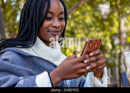 Schönes Mädchen, das sich in einem Café entspannt und in sozialen Netzwerken auf ihrem Handy chattet. Freizeit, Technologie und urbaner Lebensstil. Nahaufnahme. Stockfoto