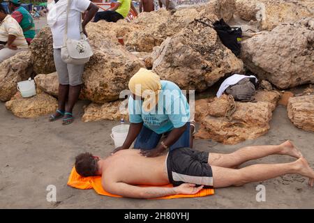 Cartagena de Indias, Kolumbien - 21. Nov 2010: Eine Frau gibt einer Touristen eine Massage, die mit dem Gesicht nach unten am Strand von Bocagrande liegt Stockfoto