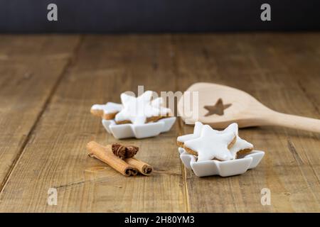 Nahaufnahme von Zimtsternen als weihnachtskekse in einer kleinen weißen Schale auf einem Holztisch, Fokus auf den Vordergrund Stockfoto