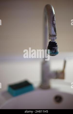 Der alte Chrom-Wasserhahn in der Küchenspüle ist mit Kalkablagerungen bedeckt. Der Schwamm der blauen Schale liegt auf einem weißen Waschbecken. Stockfoto