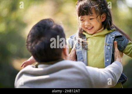 Junger asiatischer Vater umarmt 4-jährige Tochter im Freien in einem Park glücklich und lächelnd Stockfoto