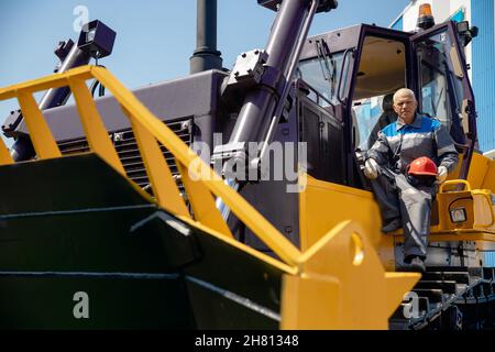 Glücklicher Fahrer Mann von industriellen Muldenkipper sitzt in der Kabine und arbeitet auf der Baustelle. Stockfoto