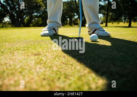 Aufnahme der Füße eines Golfspielers auf dem Loch Gras mit Ball, immer bereit, eine Schaukel mit dem Schläger zu nehmen Stockfoto