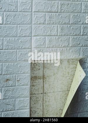 Die Tapete beginnt sich abzulösen. Die Tapete aus alten weißen Ziegeln schälte sich von der Wand im Raum, weil es feucht war oder sich nicht gut klebte. Reparieren Sie A Stockfoto