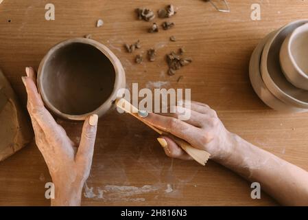 Töpferei und Werkstatt mit Tonkunst-Konzept. Nahaufnahme der Hände eines jungen Keramikers mit einem nicht gebackenen Tonkrug. Handwerklich arbeitende Hände Stockfoto