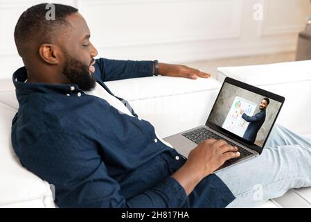 Afroamerikanischer Student Typ Angestellter beim Betrachten eines Lehrkurses auf dem Laptop, beim Studieren von zu Hause, führt ein indischer Lehrer Trainer mit Whiteboard auf dem Laptop-Bildschirm ein Business Training durch Stockfoto