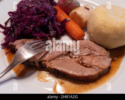 Ein Stück gebratenes Jungschweinferkelchen mit Rotkohl, Kartoffelknödel, Wintergemüse und Soße Stockfoto