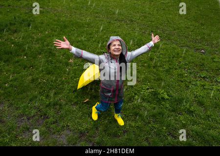 Glückliche ältere Frauen, die Spaß im Freien haben. Ältere fröhliche ältere ältere ältere Rentnerin mit gelbem Regenschirm, die das Leben an regnerischen Tagen im Park genießt. Viel Spaß Stockfoto
