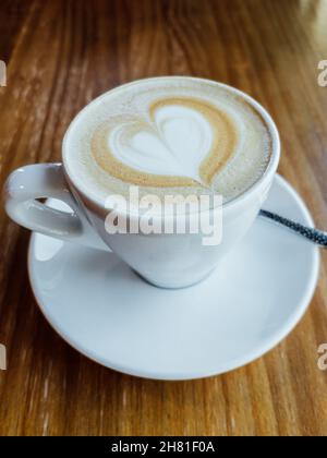 Kaffeetasse mit herzförmiger Latte-Schaumkunst auf einem Holztisch in einem Café. Stockfoto