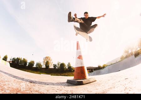 Skater-Junge, der einen Fliptrick über einem Kegel im Skatepark macht Stockfoto