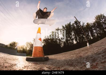 Skater-Junge, der einen Fliptrick über einem Kegel im Skatepark macht Stockfoto