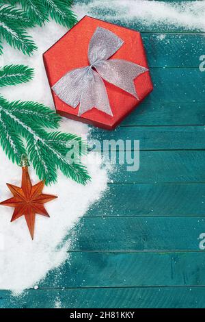 Rote Geschenkbox mit Schleife, Stern- und Tannenzweigen auf Schnee und blauen Brettern. Weihnachten, Neujahr. Speicherplatz kopieren Stockfoto