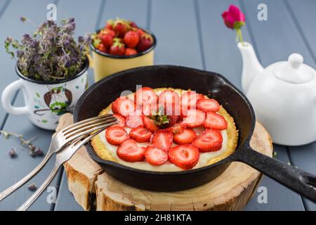 Hausgemachter Kuchen mit frischen Erdbeeren und Schlagsahne in gusseiserner Pfanne serviert mit Tee und wildem Thymian horizontal Stockfoto