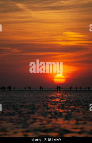 Eine Gruppe von Menschen am Strand in der Ablehung des Sonnenuntergangs vor Buesum im Wattenmeer. Stockfoto