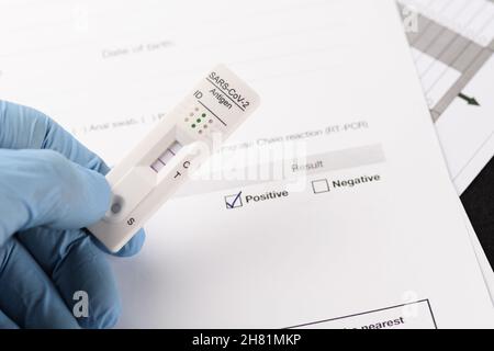 Nahaufnahme des positiven Ergebnisses durch schnellen Antigen-Test für SARS-CoV-2, COVID-19, in der Hand über Testdokument gehalten. COVID-19, Tests, Medizin, Pandem Stockfoto