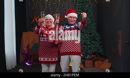 Glückliches Ehepaar aus der älteren Familie, das zu Hause Weihnachten feiert, Gläser anklirrend und Champagner trinkt Stockfoto