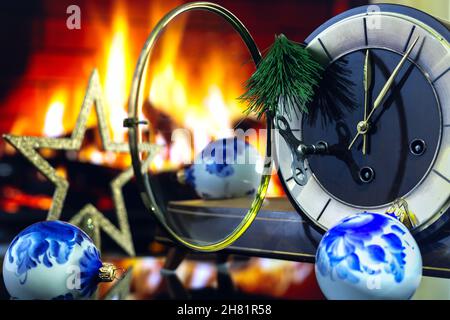 Eine Tischuhr mit einer offenen Glasabdeckung, umgeben von Weihnachtsdekorationen vor dem Hintergrund eines Feuers. Stockfoto