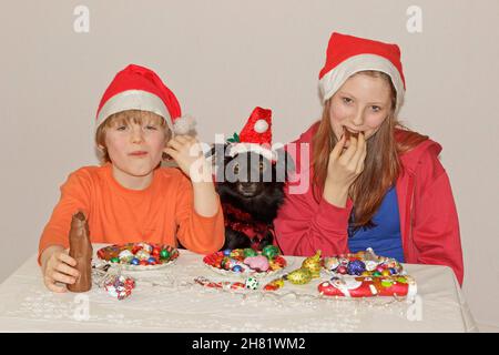 Kinder und Hund mit Weihnachtsmützen und Süßigkeiten Stockfoto