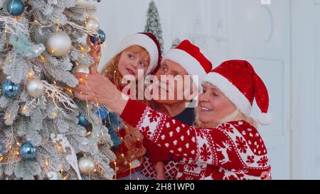 Kleinkind Mädchen mit älteren Paar Großeltern Dekoration künstliche Weihnachtskiefer zu Hause Zimmer Stockfoto