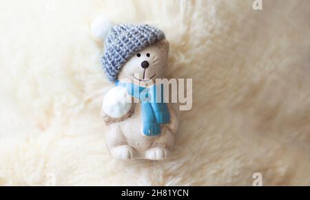 Teddybär aus Keramik in einer Kappe auf weißem, flauschigen Hintergrund. Stockfoto