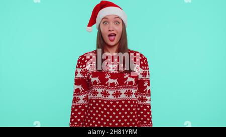 Teen erwachsenen Mädchen in Weihnachtshut Heben Hände in Überraschung schockiert durch plötzlichen Sieg, wow Emotion Stockfoto