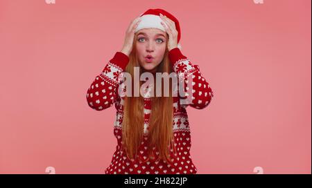 Teen erwachsenen Mädchen in Weihnachtshut Heben Hände in Überraschung schockiert durch plötzlichen Sieg, wow Emotion Stockfoto