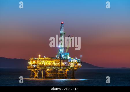 Offshore-Ölplattform vor der Küste Kaliforniens gegen einen launischen, orangen Himmel, wenn die Sonne hinter der Bohrinsel untergeht. Stockfoto