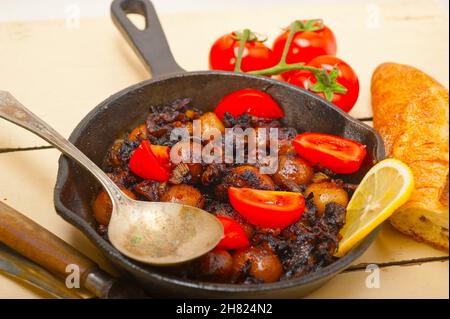 Baby Tintenfisch über rustikalen Holztisch auf eisernen Pfanne mit Tomaten und Zwiebeln gebraten Stockfoto