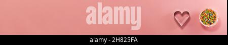 Banner von Cupcake-Linern mit farbigem Zucker innen und herzförmigem Cutter unten von oben. Flach liegend, Draufsicht. Süßwarenkonzept mit Kopie sp Stockfoto