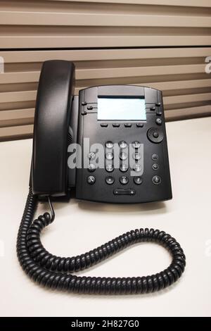 Schwarzes Büro-IP-Telefon auf dem Schreibtisch der Bürokabine Stockfoto