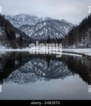 Faszinierende Szene von felsigen schneebedeckten Bergen unter einem trüben Himmel, die sich auf einem Wassersee spiegeln Stockfoto