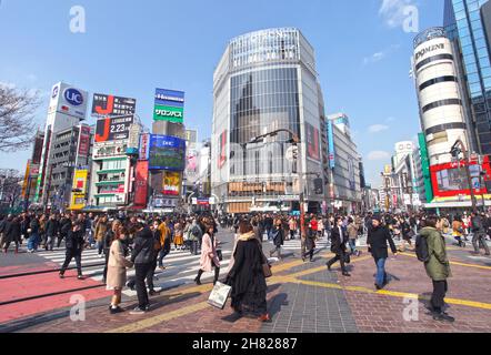 Shibuya Crossing auch bekannt als Shibuya Intersection und Shibuya Scramble in Tokio mit vielen Menschen, die die Kreuzung an einem sonnigen Tag überqueren. Stockfoto