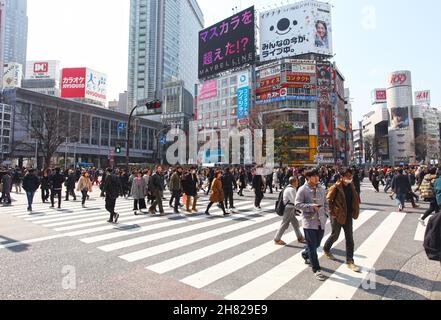 Shibuya Crossing auch bekannt als Shibuya Intersection und Shibuya Scramble in Tokio mit vielen Menschen, die die Kreuzung an einem sonnigen Tag überqueren. Stockfoto