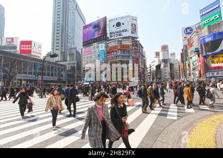 Shibuya Crossing auch bekannt als Shibuya Intersection und Shibuya Scramble in Tokio mit vielen Menschen, die die Kreuzung an einem sonnigen Tag überqueren. Stockfoto