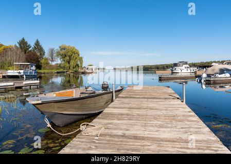 Das Motorboot vertäute an einem verwitterten hölzernen Steg in einem Flusshafen an einem klaren Herbsttag, einer ruhigen Szene. Stockfoto