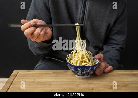 Spaghetti mit Essstäbchen halten und mit den Händen eines Jungen aus einer blauen Schüssel ziehen Stockfoto